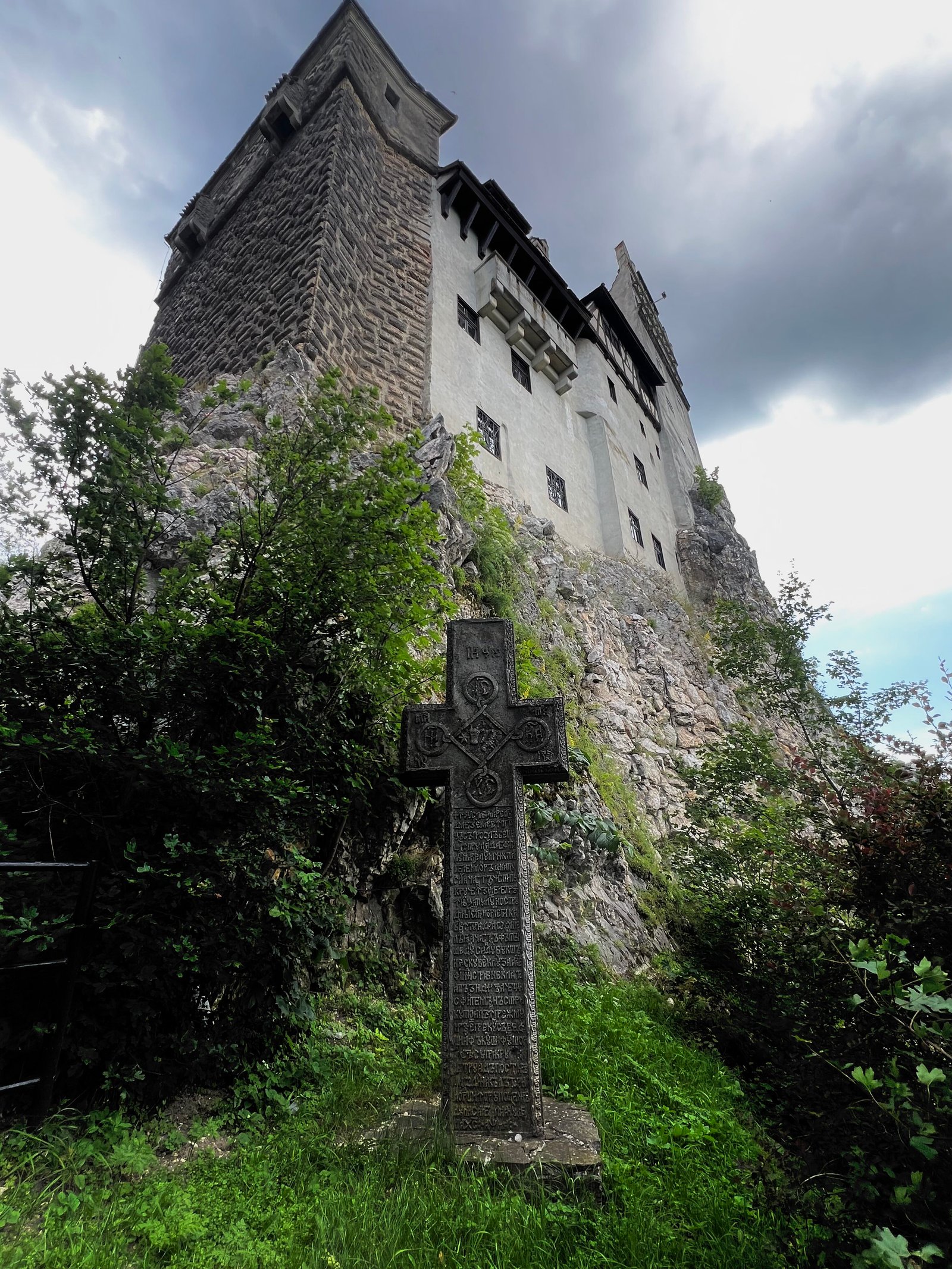 An image of Bran Castle perched on a cliff with a cross standing tall in front of it.